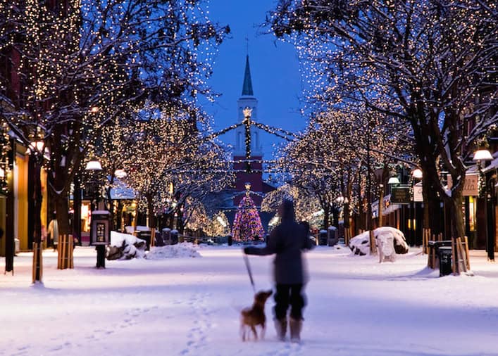 Brightly illuminated winter street scene with snow-covered trees and festive holiday lights, showcasing a cozy, picturesque holiday atmosphere.
