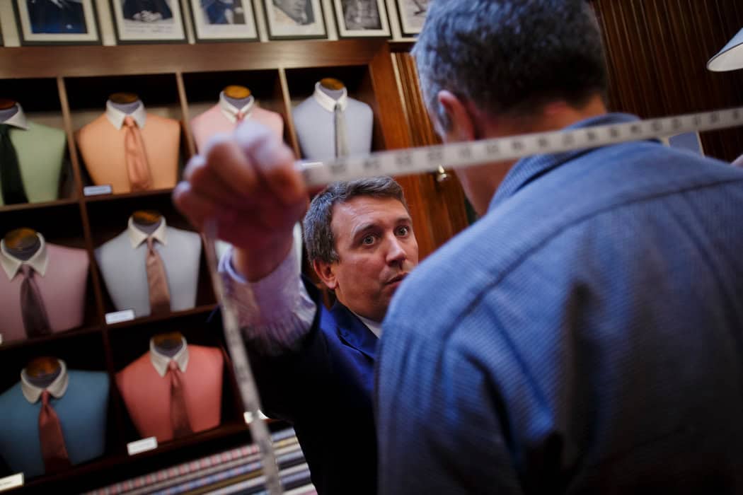 Tailor measuring a customer's shoulder width for a custom dress shirt at DeoVeritas, men's tailoring store.