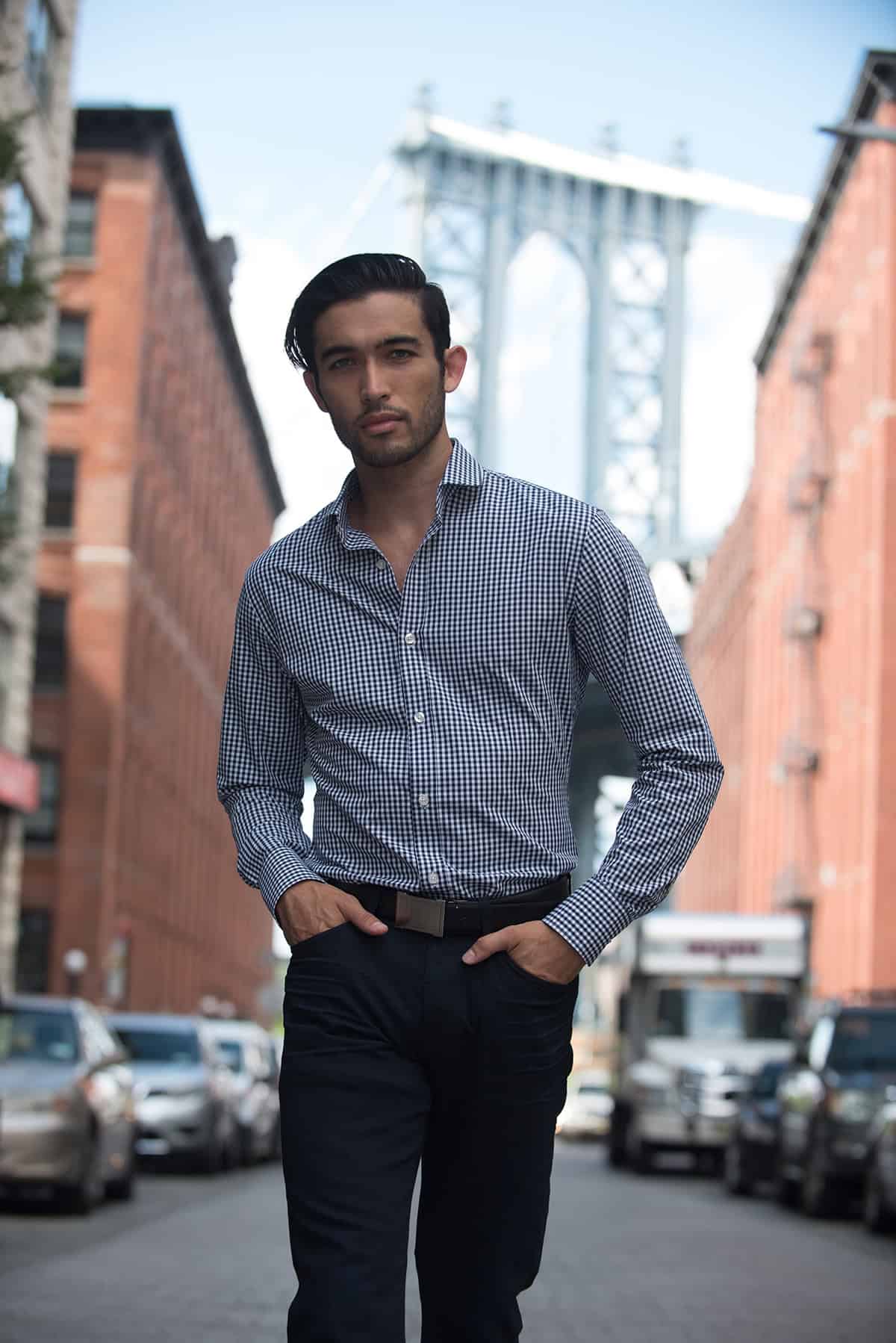 Stylish man in a checkered dress shirt walking in an urban city street near the Brooklyn Bridge in New York, showcasing men's fashion and business casual style for city life.
