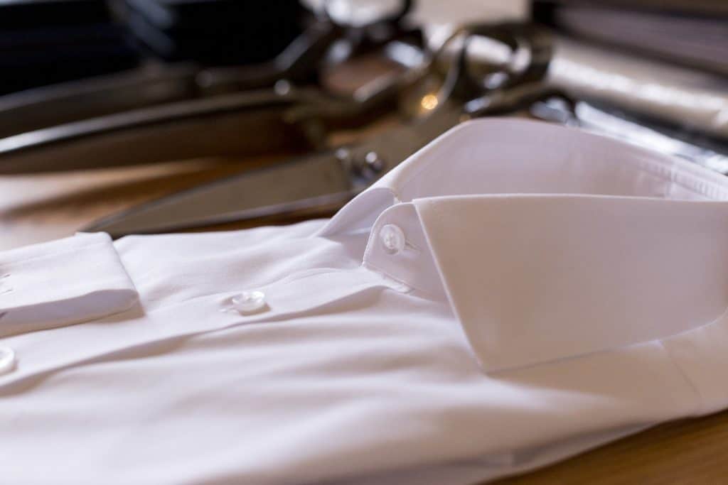 Elegant white dress shirt neatly folded with buttons, lying on a wooden surface with other clothing items in the background, ideal for formal occasions or professional attire.