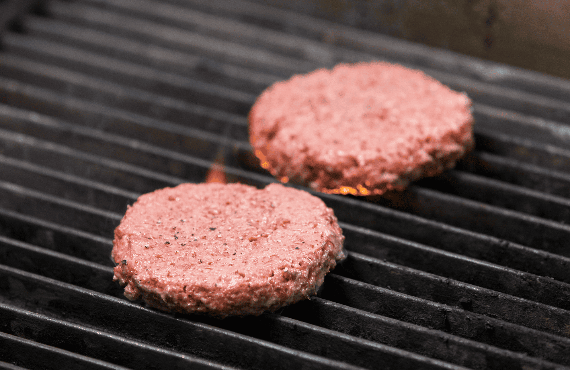 Juicy raw hamburger patties cooking on a grill, ready to be flipped for perfect burger preparation. Focus on grilling beef patties for delicious homemade burgers.