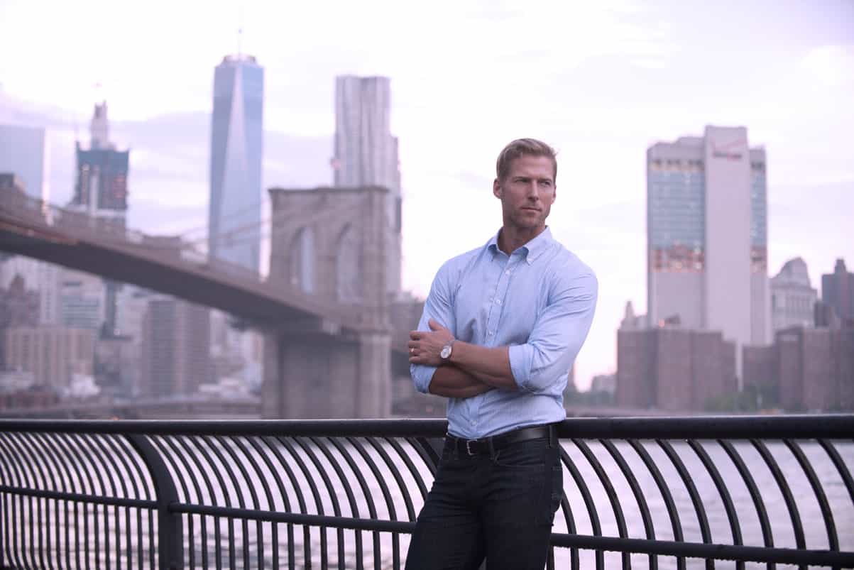 Stunning cityscape background featuring a confident man in business attire standing by the waterfront with Brooklyn Bridge and Manhattan skyline in NYC.