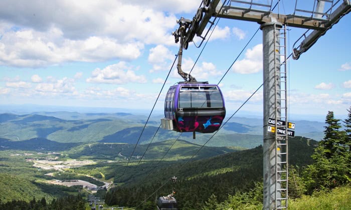 Cable car ascending over lush green mountains and valleys with blue skies and scattered clouds, capturing scenic views and outdoor adventures.