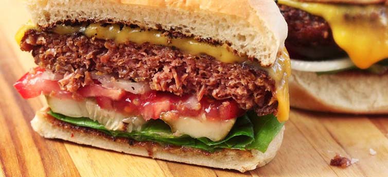 Crispy beef burger with fresh vegetables and melted cheddar cheese on a toasted bun, close-up shot.