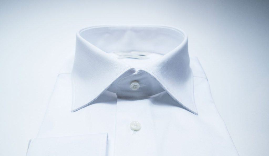 A classic white dress shirt with a spread collar and buttons, neatly laid out with reflections on a white surface, symbolizing professionalism and elegance.