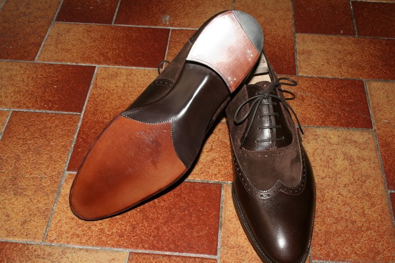 Polished men's leather dress shoes with brogue detailing on a tiled floor, showcasing high-quality craftsmanship and elegant style.