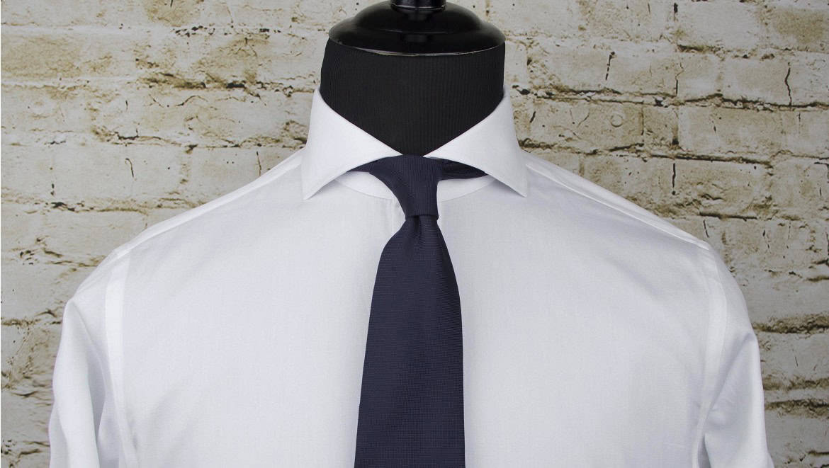 Elegant white dress shirt with navy tie on mannequin against rustic brick wall, showcasing men's formal apparel for business or special occasions.