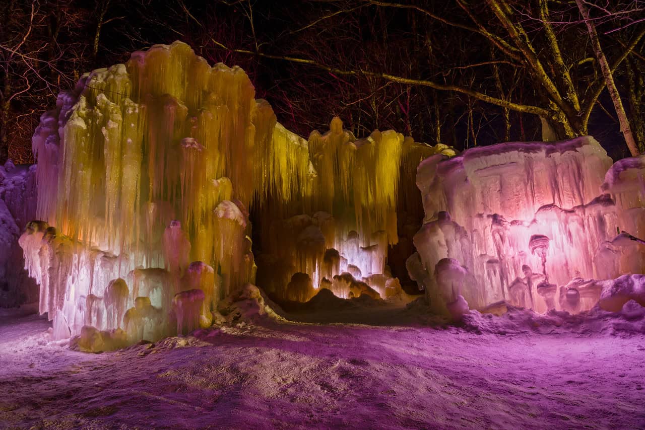 Colorful ice formations at night illuminated with vibrant pink, yellow, and purple lights, creating a stunning winter ice sculpture scene perfect for outdoor winter adventures and ice art photography.