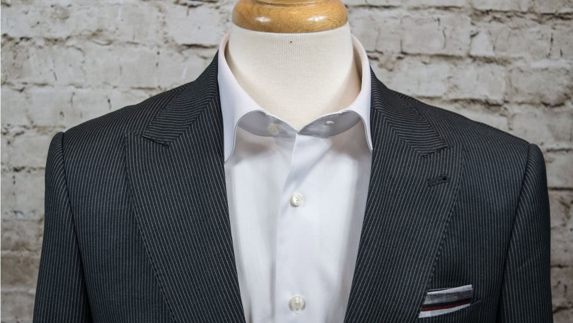 Sharp tailored men's suit with white dress shirt on mannequin against brick wall background, perfect for business or formal occasions.