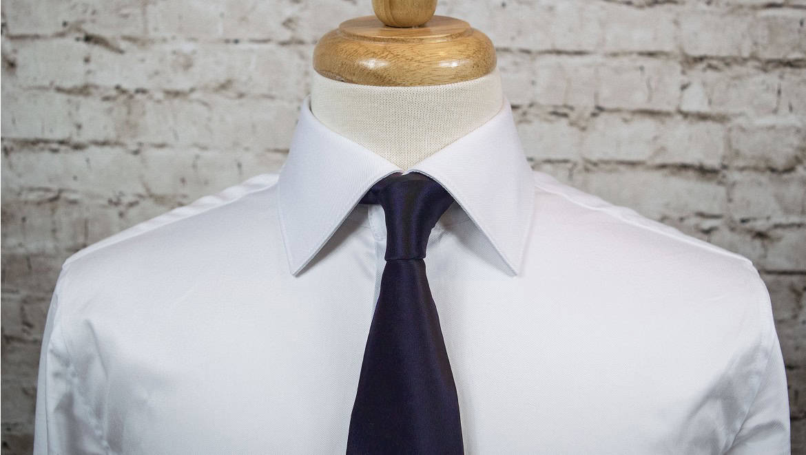 Elegant white dress shirt with navy blue tie on mannequin, ideal for formal occasions, business attire, or professional settings. Perfect for those seeking stylish and sophisticated men's fashion.