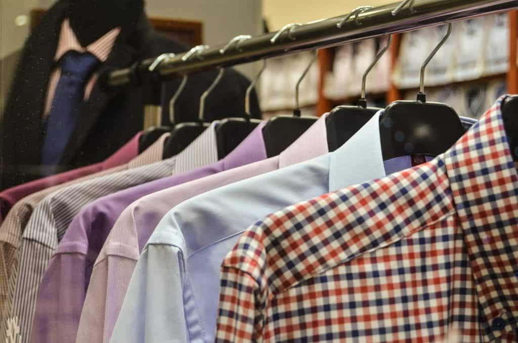 Brightly colored men's dress shirts on hangers in a clothing store, showcasing a variety of striped, solid, and checked patterns for formal and casual wear.