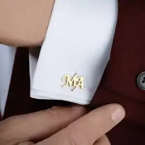 "Elegant gold monogram cufflink with initials 'M' and 'A' worn on a white shirt cuff, showcasing sophisticated men's accessories for formal or business attire.".