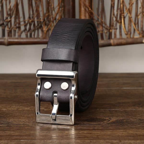 Leather belt with silver buckle on wooden surface, close-up of men's fashion accessory.