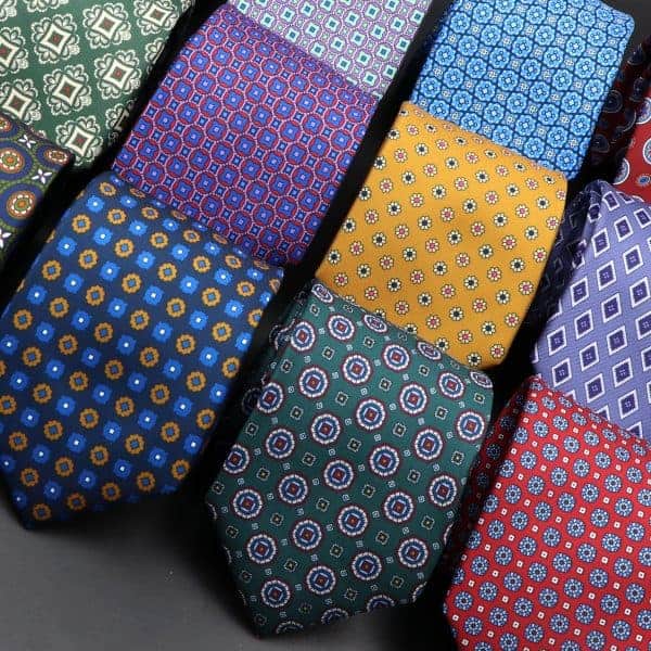 Colorful patterned neckties featuring geometric and floral designs in blue, green, yellow, red, and purple tones arranged in a diagonal display.