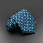 Colorful patterned men's silk tie with geometric floral design in blue, green, and navy for formal occasions and professional attire.