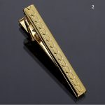 Gold tie clip with textured geometric pattern on a reflective dark surface.
