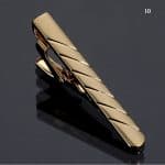 Shiny gold tie clip with diagonal striped design on reflective black surface.