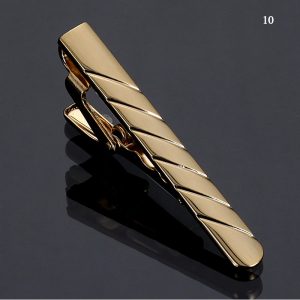 Shiny gold tie clip with diagonal striped design on reflective black surface.