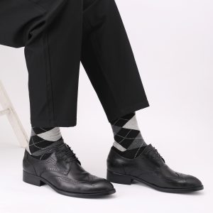Polished black leather dress shoes with brogue detailing, paired with gray argyle socks and black tailored trousers, perfect for formal or business attire.