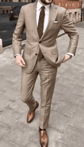 Elegant man in tailored beige suit walking on city street, showcasing professional business attire and stylish dress shoes.