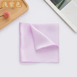 Light pink silk pocket square neatly folded on white surface, with magazine and wooden tray with pink decorative item in background at DeoVeritas.