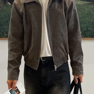A brown leather jacket worn by a person holding a pamphlet and a black tote bag, standing against a blurred outdoor background, displaying a stylish and timeless fashion choice.