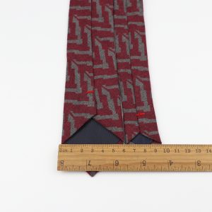 Polyester necktie with abstract geometric pattern in red and gray, featuring black silk interior lining, measured with wooden ruler for precise length, ideal for stylish menswear accessories.