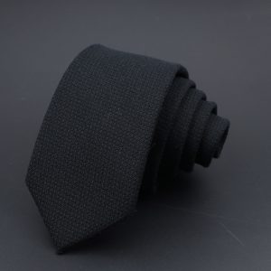 Dark black men's dress tie, neatly rolled on a dark background, showcasing elegant and professional men's fashion accessories for formal occasions.